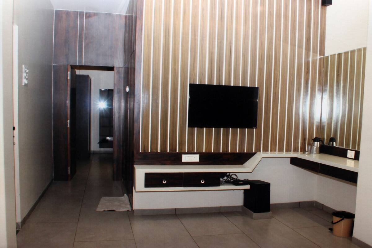 A modern bathroom with a large mirror, a flat-screen TV mounted on a wooden panel wall, and a built-in vanity with a sink and storage.