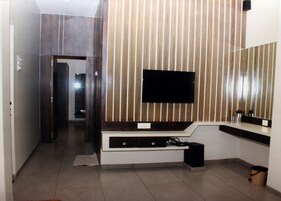 Un baño moderno con un espejo grande, un televisor de pantalla plana montado en una pared de paneles de madera y un tocador empotrado con lavamanos y espacio de almacenamiento.