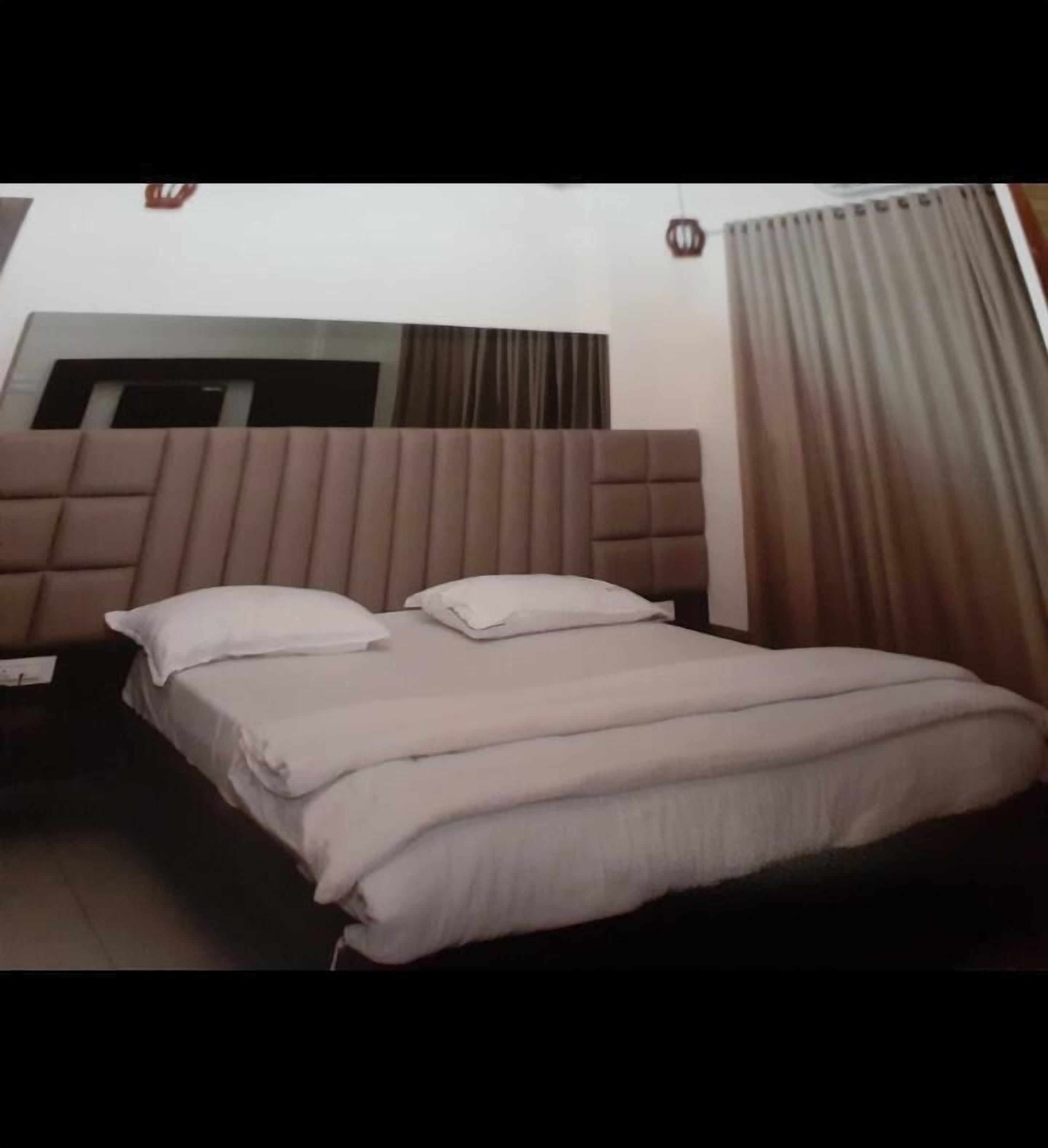 Quarto de hotel com cama, cabeceira, mesa de cabeceira e janela com cortinas.