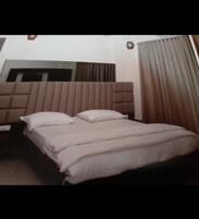 Quarto de hotel com cama, cabeceira, mesa de cabeceira e janela com cortinas.