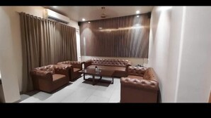 A living room with a brown leather sectional sofa, a glass coffee table, and a ceiling fan. - Hotel Central Park (Ambernath)