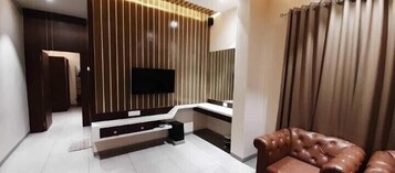 Una sala de estar moderna con un televisor de pantalla plana montado en una pared de madera, un sofá y un ventanal con cortinas.