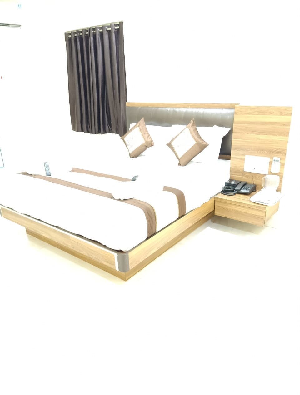 Uma cama moderna com estrutura de madeira, painel de cabeceira e mesa de cabeceira com telefone e luminária.