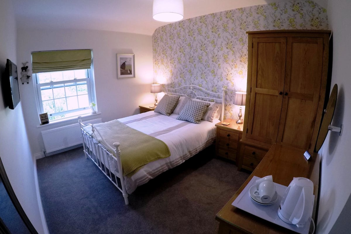 Quarto com cama, mesas de cabeceira, guarda-roupa, janela e radiador.