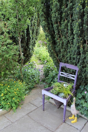 A garden with a purple bench, a wooden duck sculpture, and various plants. - The Vine B & B (Alford)
