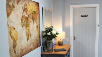Un couloir orné d’une carte du monde, une console en bois avec une lampe, et une porte donnant accès à un espace privé.