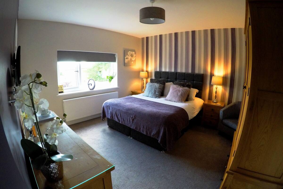 Quarto com cama, luminárias de cabeceira, janela com vista e um vaso com flores.