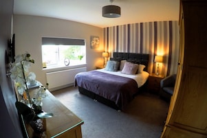 Quarto com cama, luminárias de cabeceira, janela com vista e um vaso com flores.