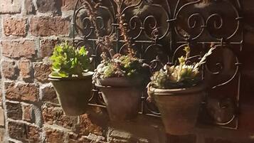 A brick wall with three potted plants on a metal bracket.
