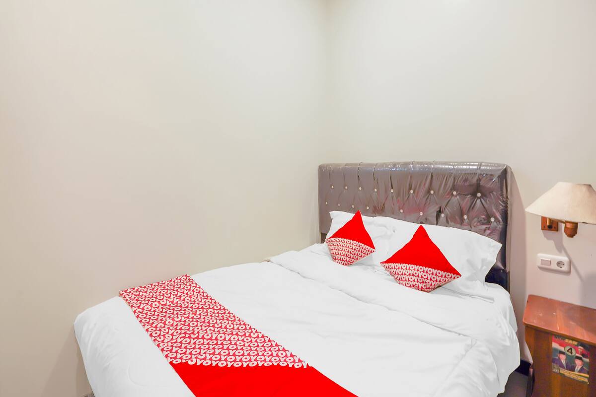A neatly made bed with a white and red bedspread, two red pillows, and a grey upholstered headboard.