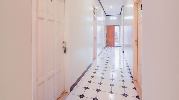 A hallway with white walls, a tiled floor, and a wooden door at the end. - Hotel O Gangnam Style Residence (Surabaya)