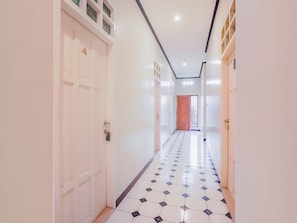 Um corredor com paredes brancas, chão de azulejos e uma porta de madeira no final.