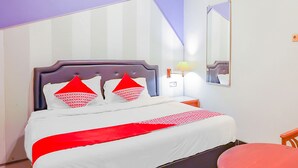 A neatly made bed with white bedding and red accents, a bedside table with a lamp, and a small round table with a red top. - Hotel O Gangnam Style Residence (Surabaya)