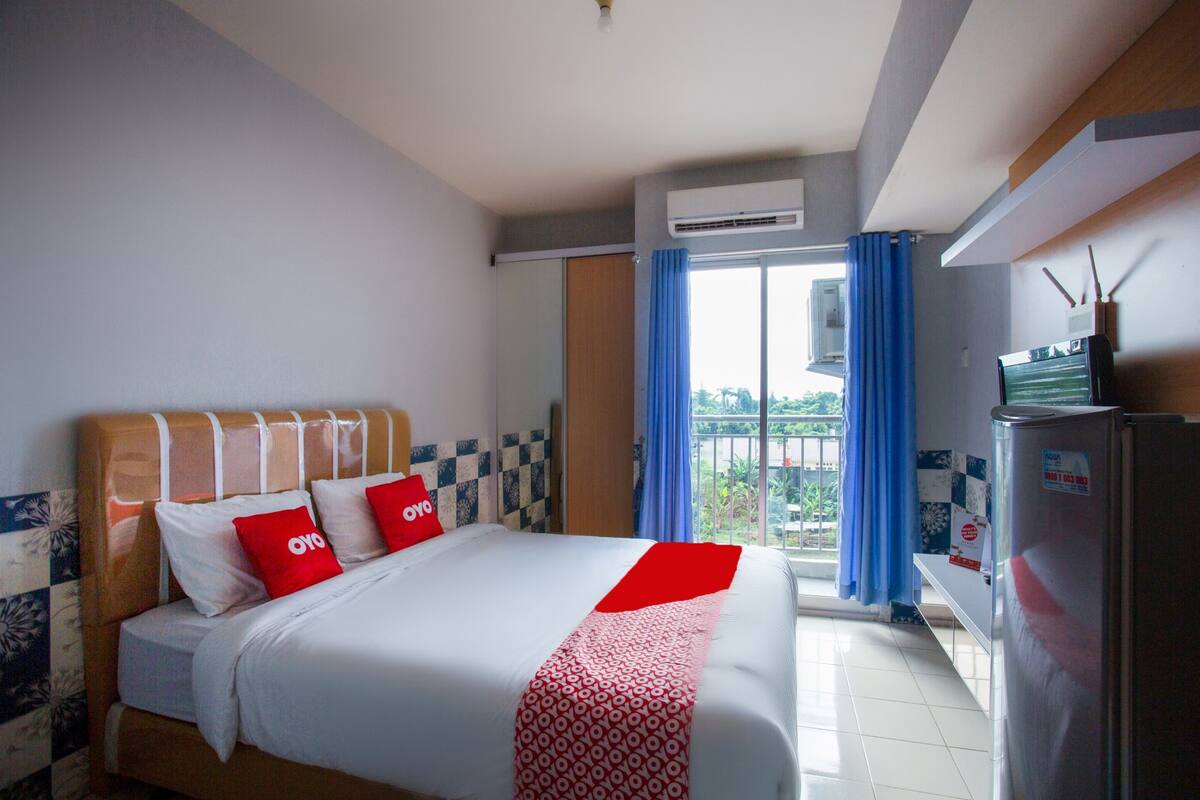 A hotel room with a bed, a refrigerator, and a window with curtains.