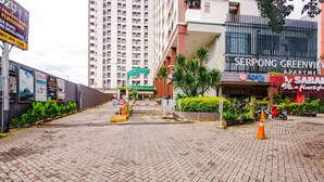 A gated entrance to Serpong Greenview apartment complex with a paved pathway, a green archway, and a storefront with signage for 'Agery' and 'Sabah'. - OYO 2582 Apartemen Serpong Green View (South Tangerang)
