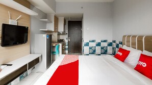 A modern hotel room with a bed, a TV, a desk, and a kitchenette. - OYO 2582 Apartemen Serpong Green View (South Tangerang)
