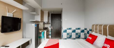 A modern hotel room with a bed, a TV, a desk, and a kitchenette.