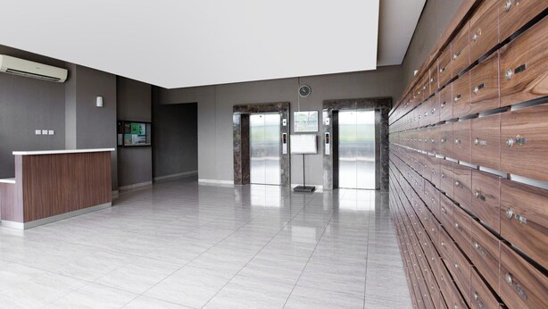 A modern lobby with a reception desk, elevators, and a row of wooden lockers. - OYO 2582 Apartemen Serpong Green View (South Tangerang)