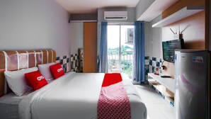 A hotel room with a bed, a desk, an air conditioner, a refrigerator, and a window with curtains. - OYO 2582 Apartemen Serpong Green View (South Tangerang)