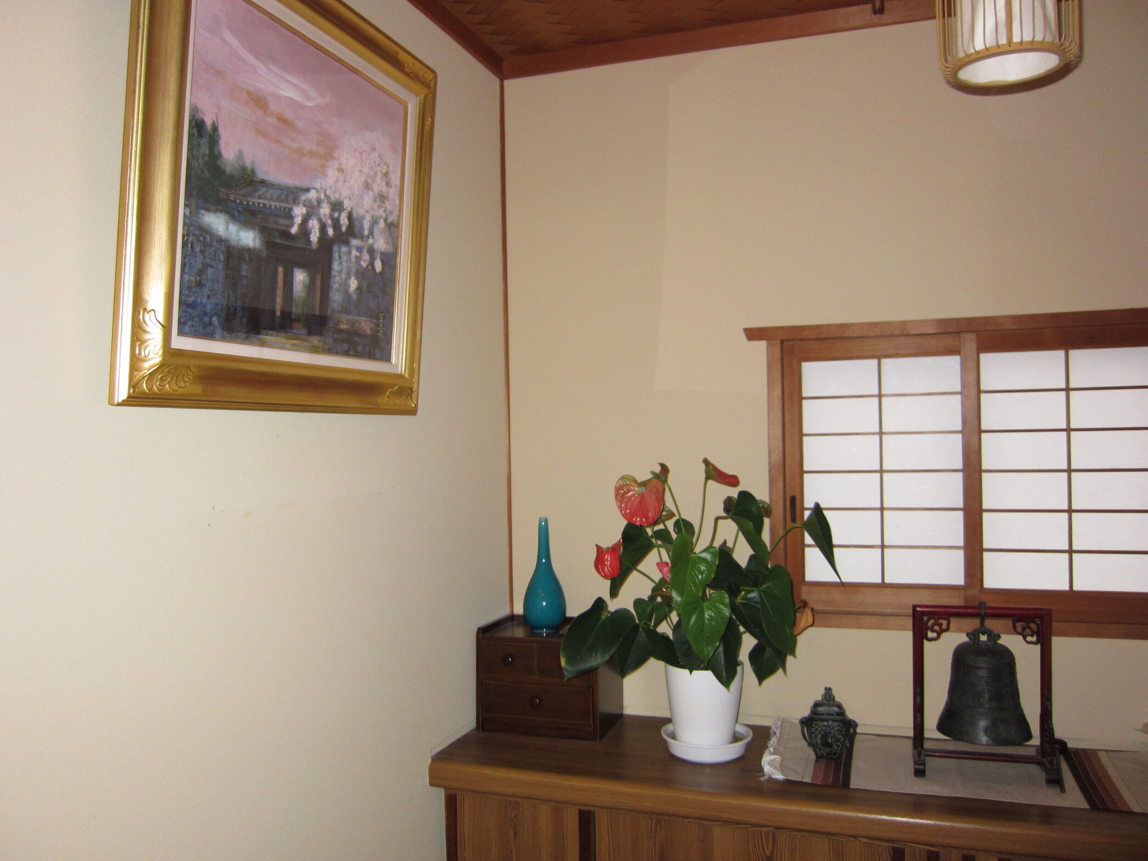 Une commode en bois sur laquelle sont posés un vase de fleurs, un tableau encadré et une cloche.