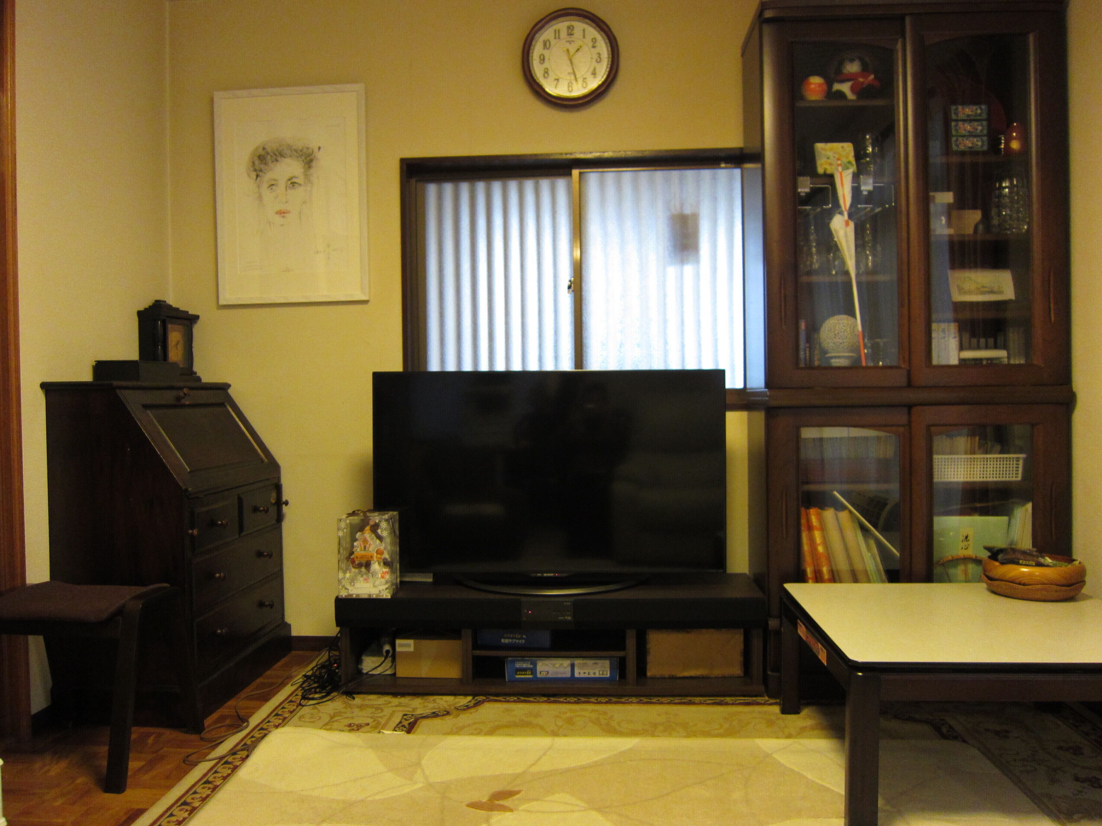 A living room with a television, a clock, a cabinet, and a framed picture on the wall.
