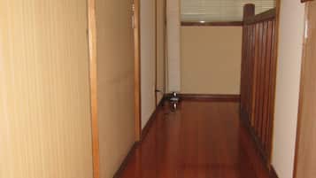A narrow hallway with wooden flooring, a wooden railing on one side, and a window with blinds in the background.