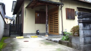Una casa tradicional japonesa con entrada de madera, un porche cubierto y un pequeño jardín.