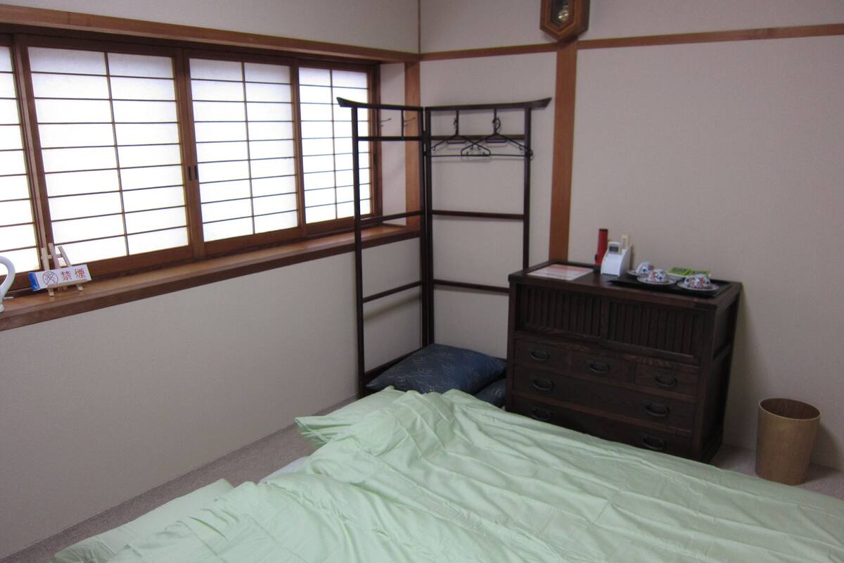 A room with a bunk bed, a dresser, a window with a wooden frame, and a small shelf with items.