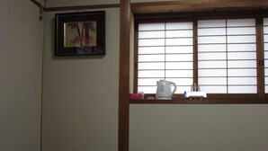 Una habitación con suelo de tatami, una mesa baja con un hervidor, un cuadro en la pared y una ventana con celosías shoji.