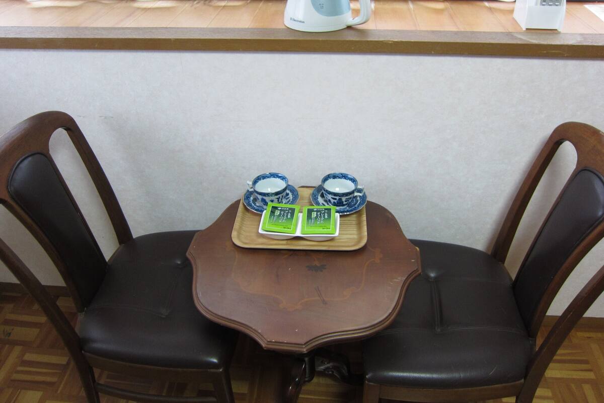 A wooden table with two blue and white cups and a tray with two green cards, set between two chairs.