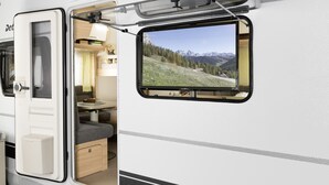 A white RV interior with a mounted TV displaying a mountainous landscape. - Ferienpark Auf dem Simpel (Soltau)