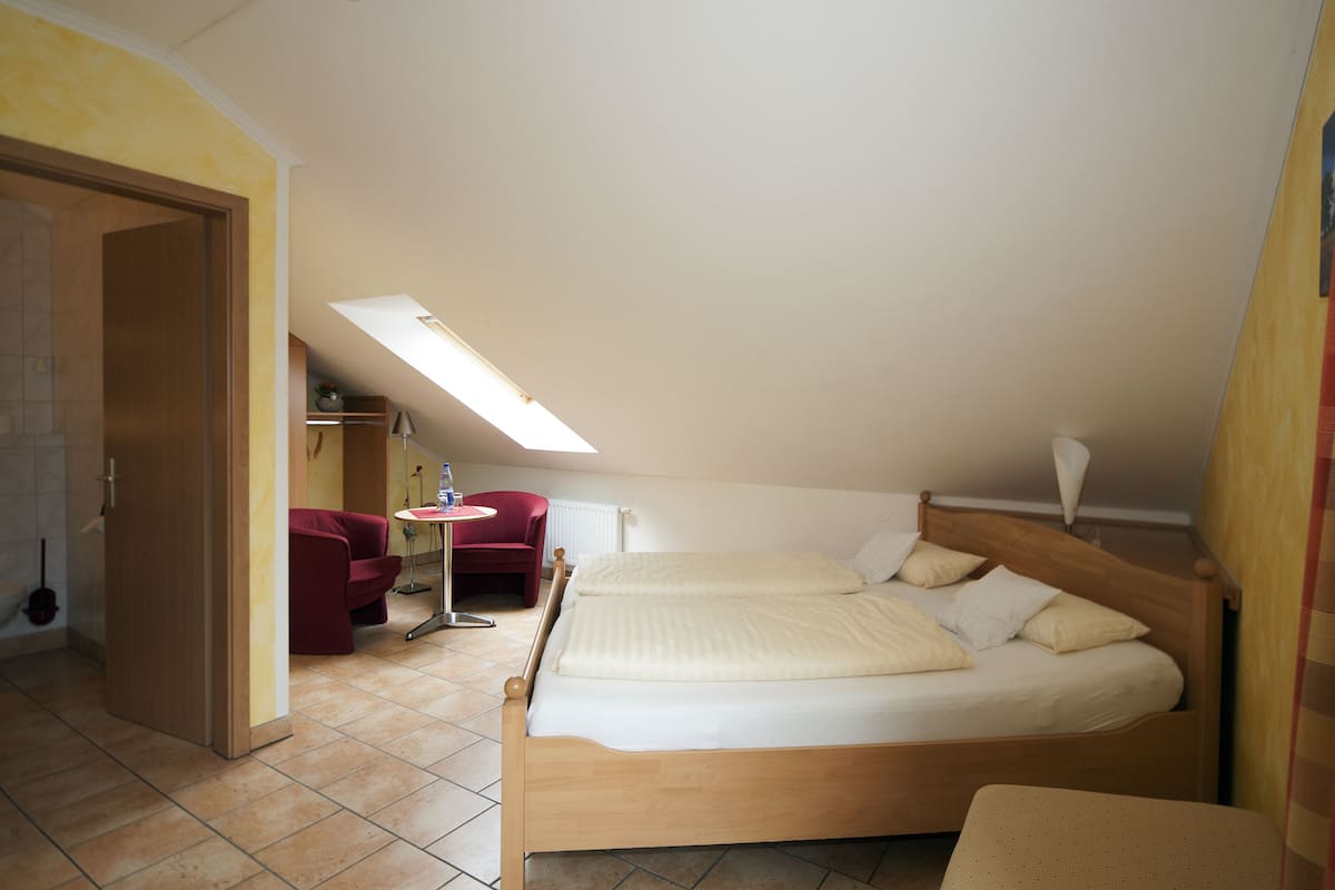 A bedroom with a wooden bed, a red chair, a small table, and a skylight.