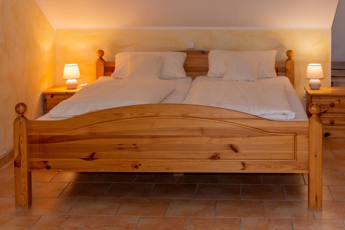 A wooden bed with two nightstands, each with a lamp, in a room with tiled flooring.