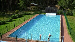 A rectangular swimming pool with clear blue water, surrounded by a brick walkway and green fencing. - Ferienpark Auf dem Simpel (Soltau)