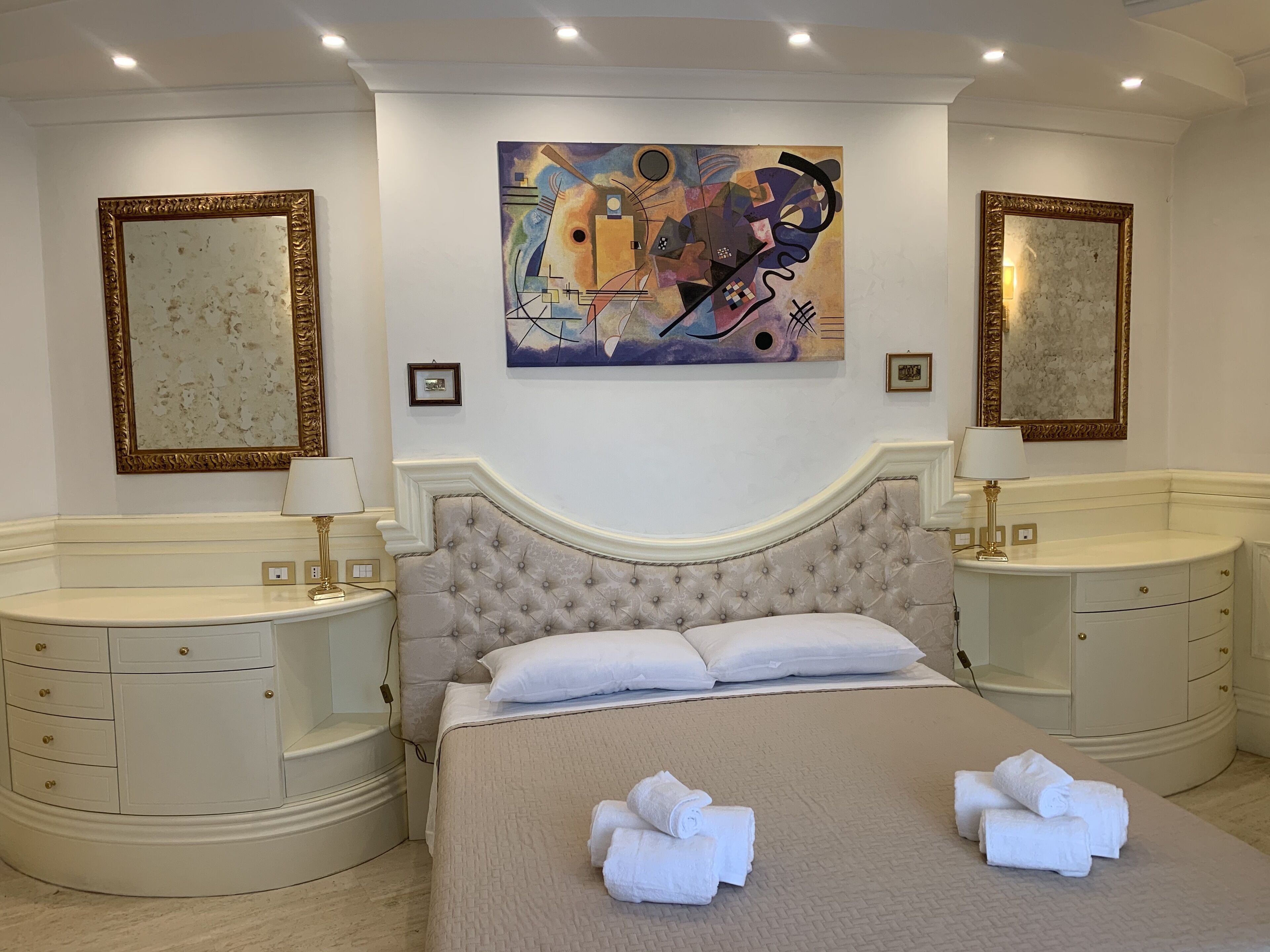 Habitación de hotel con una cama grande, dos mesitas de noche, un cabecero y dos espejos adosados a la pared.