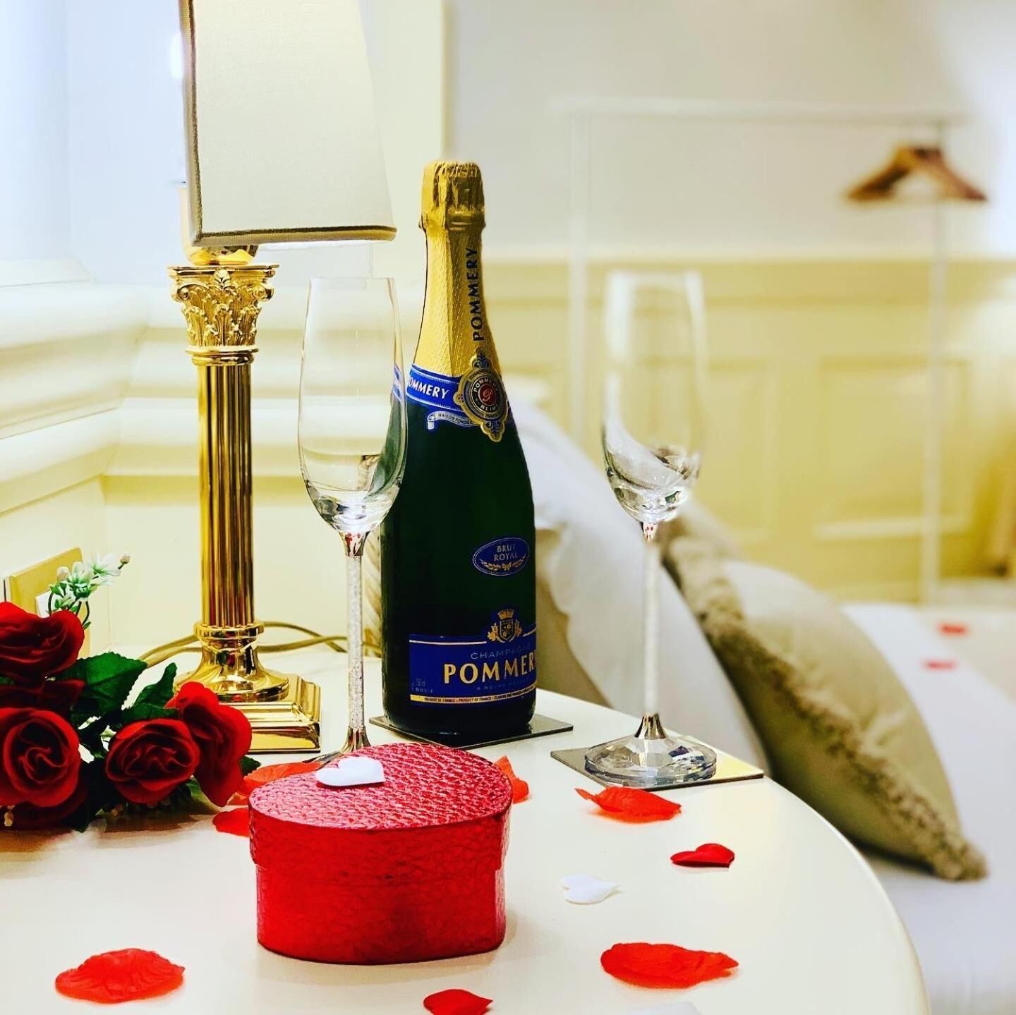 Ein Tisch mit einer Champagnerflasche, zwei Gläsern, einem roten Kerzen und roten Rosenblüten.