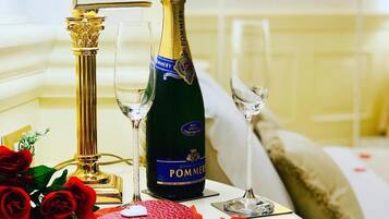 Une table avec une bouteille de champagne, deux verres, une bougie rouge et des pétales de rose rouges.