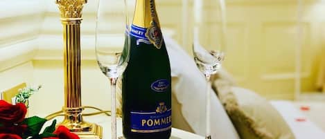 Ein Tisch mit einer Champagnerflasche, zwei Gläsern, einem roten Kerzen und roten Rosenblüten.