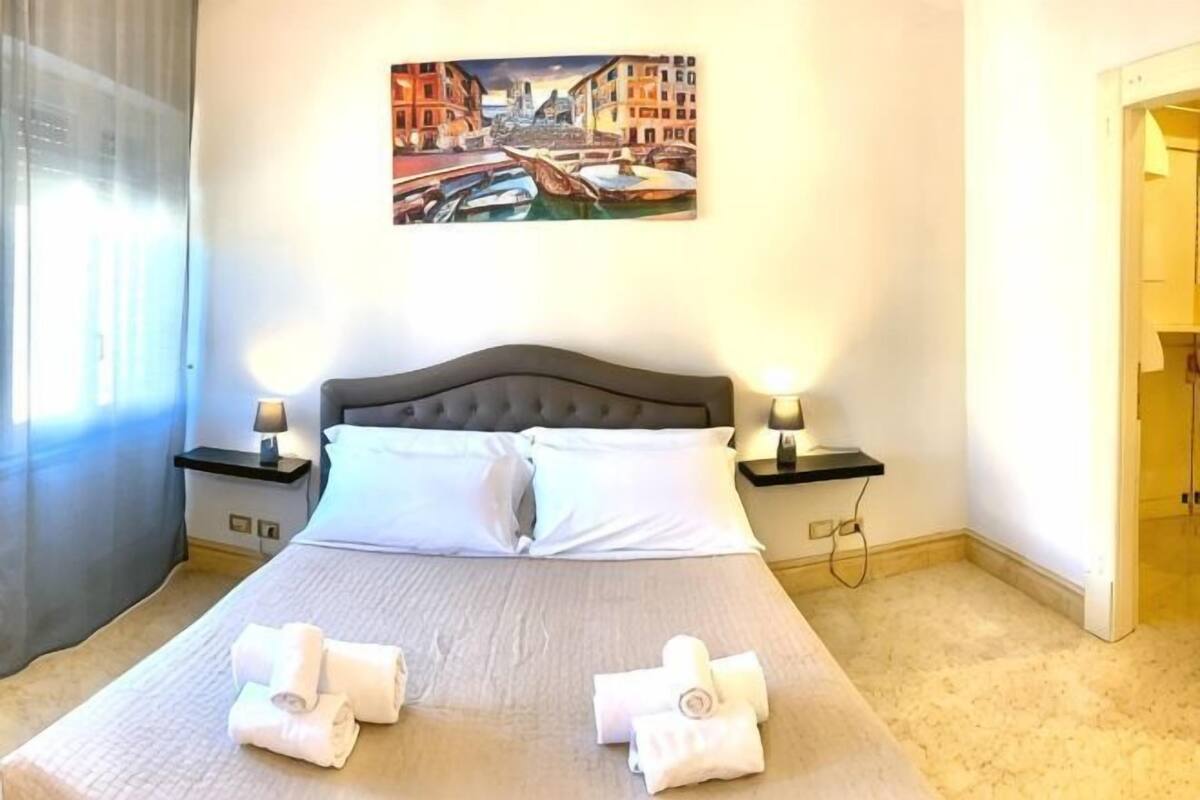 A neatly made bed with two pillows, a painting of a cityscape on the wall, and two bedside lamps.