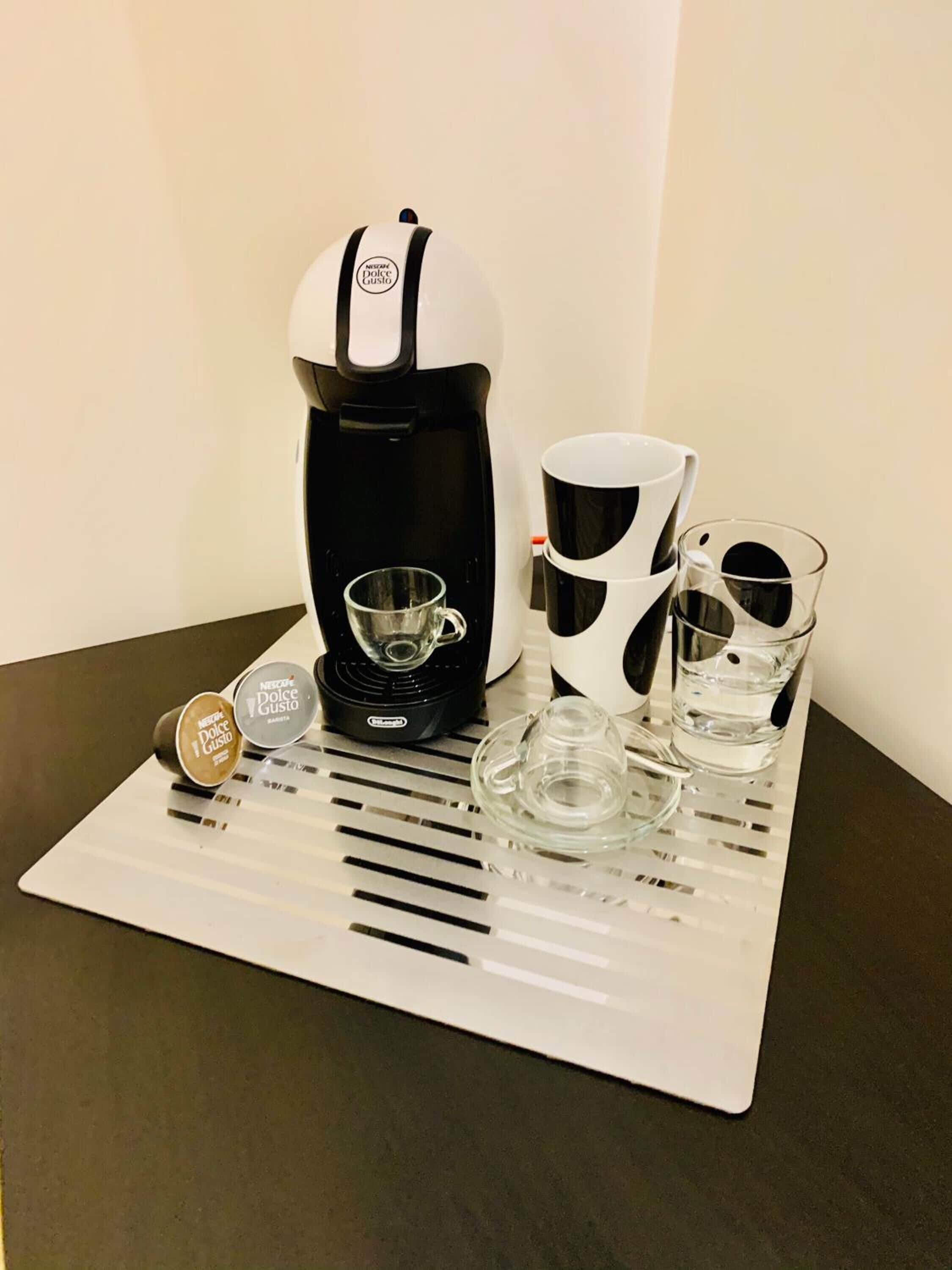 Une machine à café, deux tasses et un verre sur un plateau.
