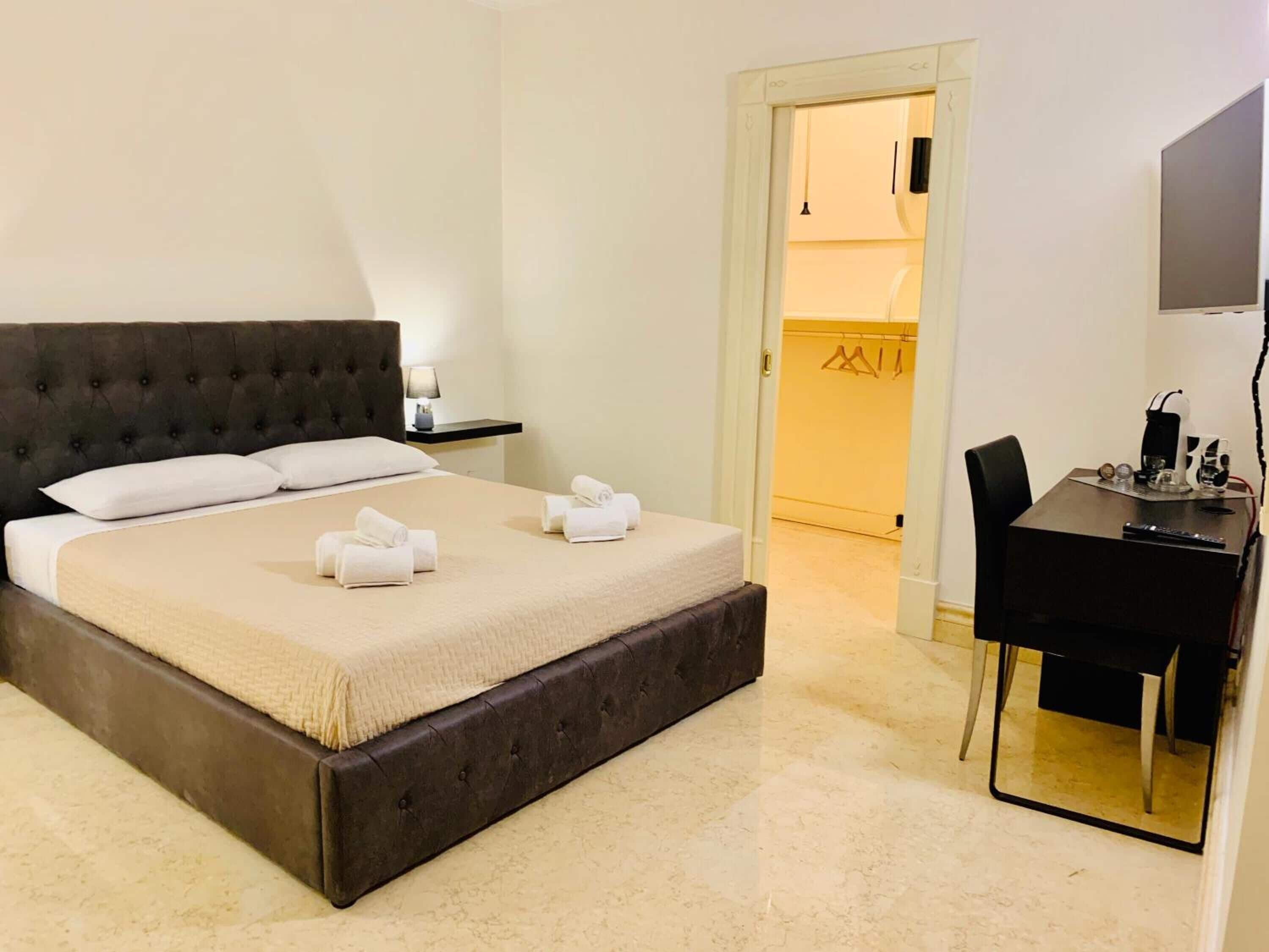A hotel room with a large bed, a desk with a chair, a TV, and a door leading to a bathroom.