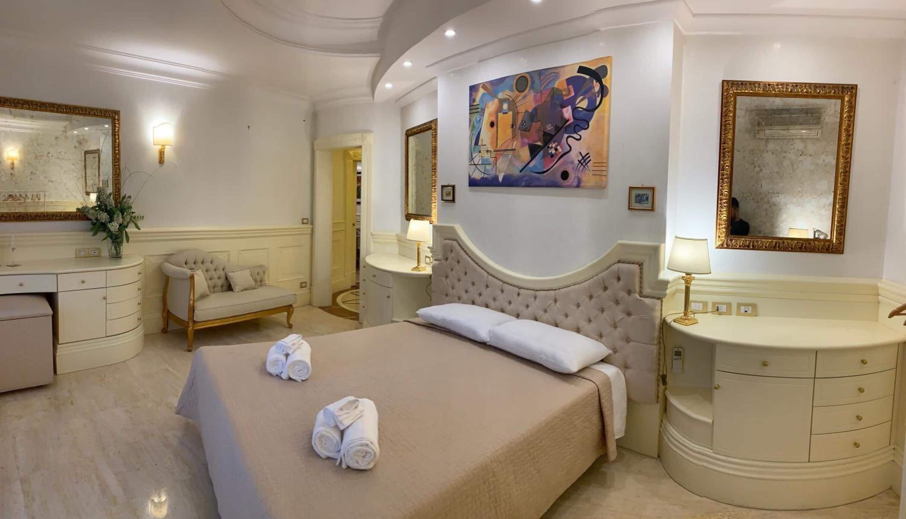 Une chambre d’hôtel avec un grand lit, une coiffeuse avec un miroir, une chaise et un tableau au mur.