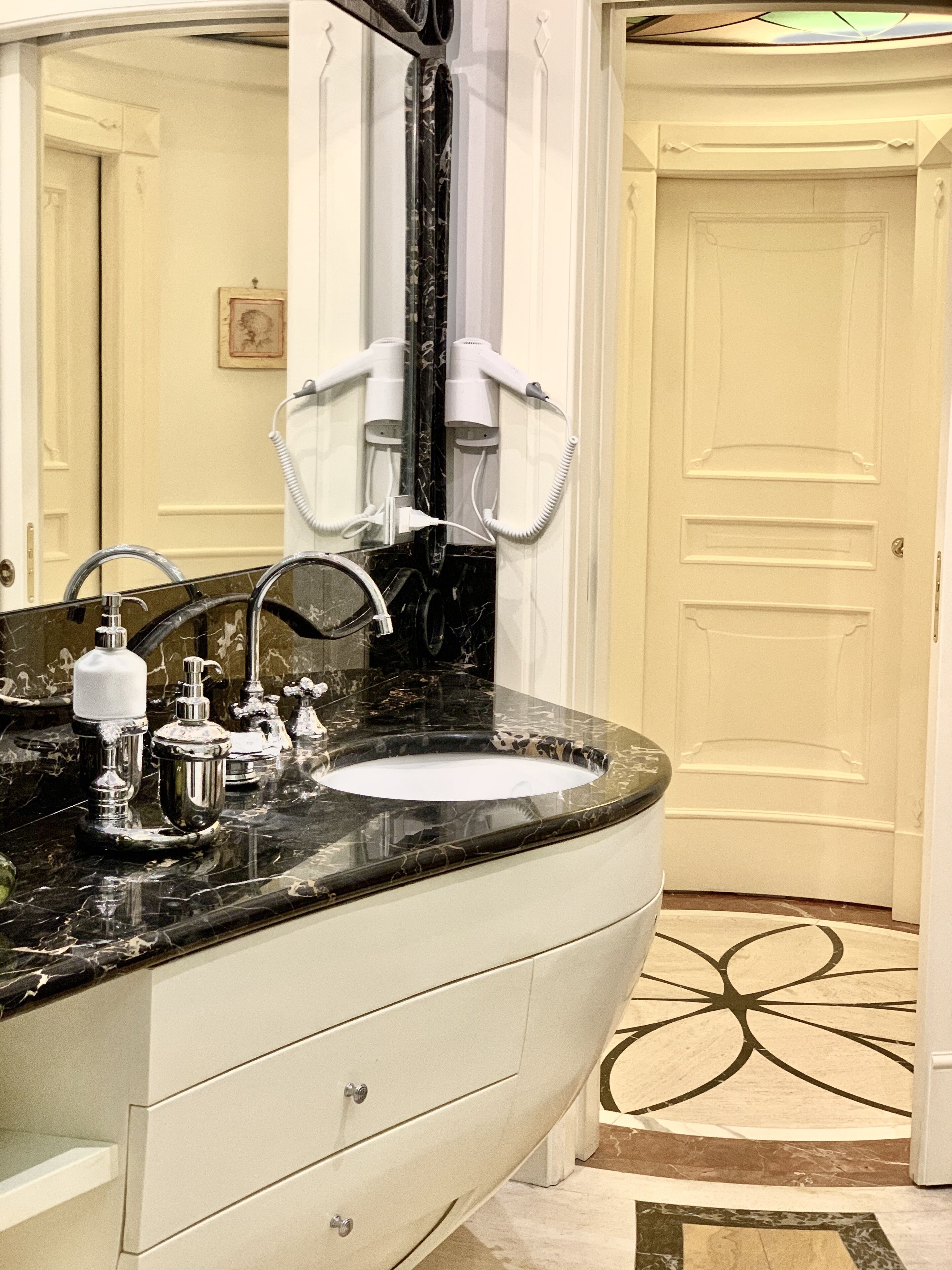 Une salle de bain avec un grand meuble-lavabo, un évier et un miroir. Deux sèche-cheveux sont fixés au mur.