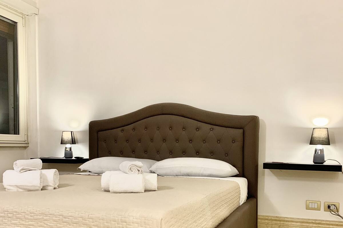 A neatly made bed with a brown headboard, white linens, and two bedside lamps on matching nightstands.