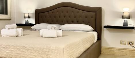 A neatly made bed with a brown headboard, white linens, and two bedside lamps on matching nightstands.