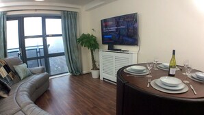 Un salon comprenant un canapé, une table à manger dressée pour quatre personnes, une plante en pot et un téléviseur fixé au mur.