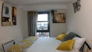 Une chambre à coucher avec un lit, deux oreillers, un radiateur et des œuvres d’art accrochées aux murs.