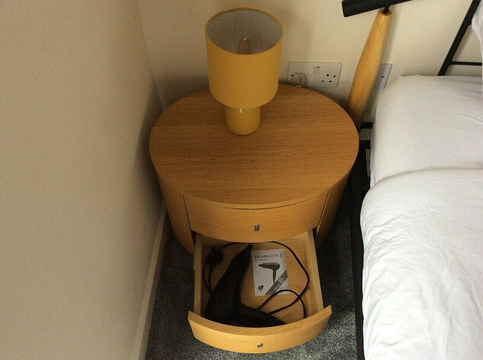Ein Nachttisch aus Holz mit einer Lampe, einer Schublade und einer Steckdose.
