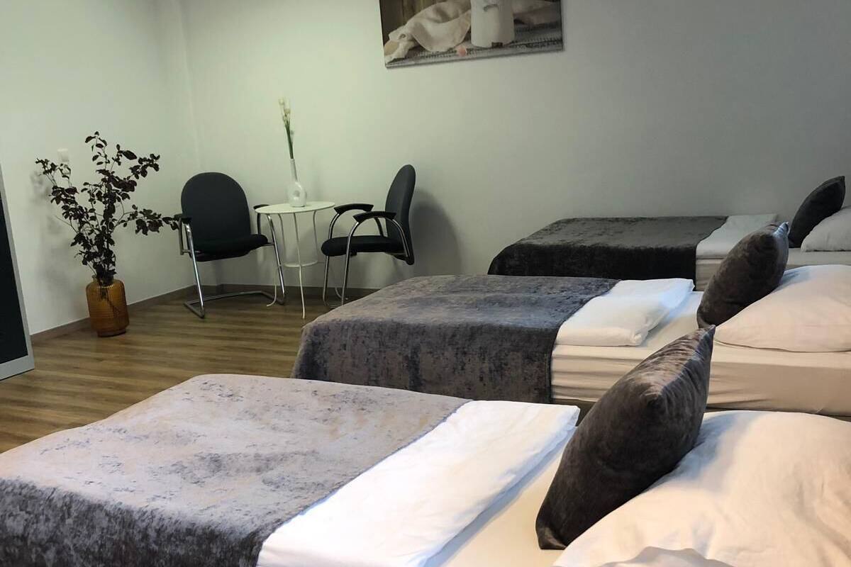 A hotel room with two beds, a small table with chairs, a potted plant, and a painting on the wall.
