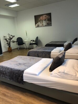 A hotel room with two beds, a small table with chairs, a potted plant, and a painting on the wall. - Hostel Messe Laatzen (Laatzen)